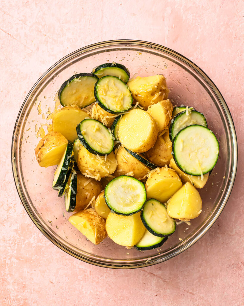 Zucchini rounds and baby potatoes in a bowl mixed in seasoning. 