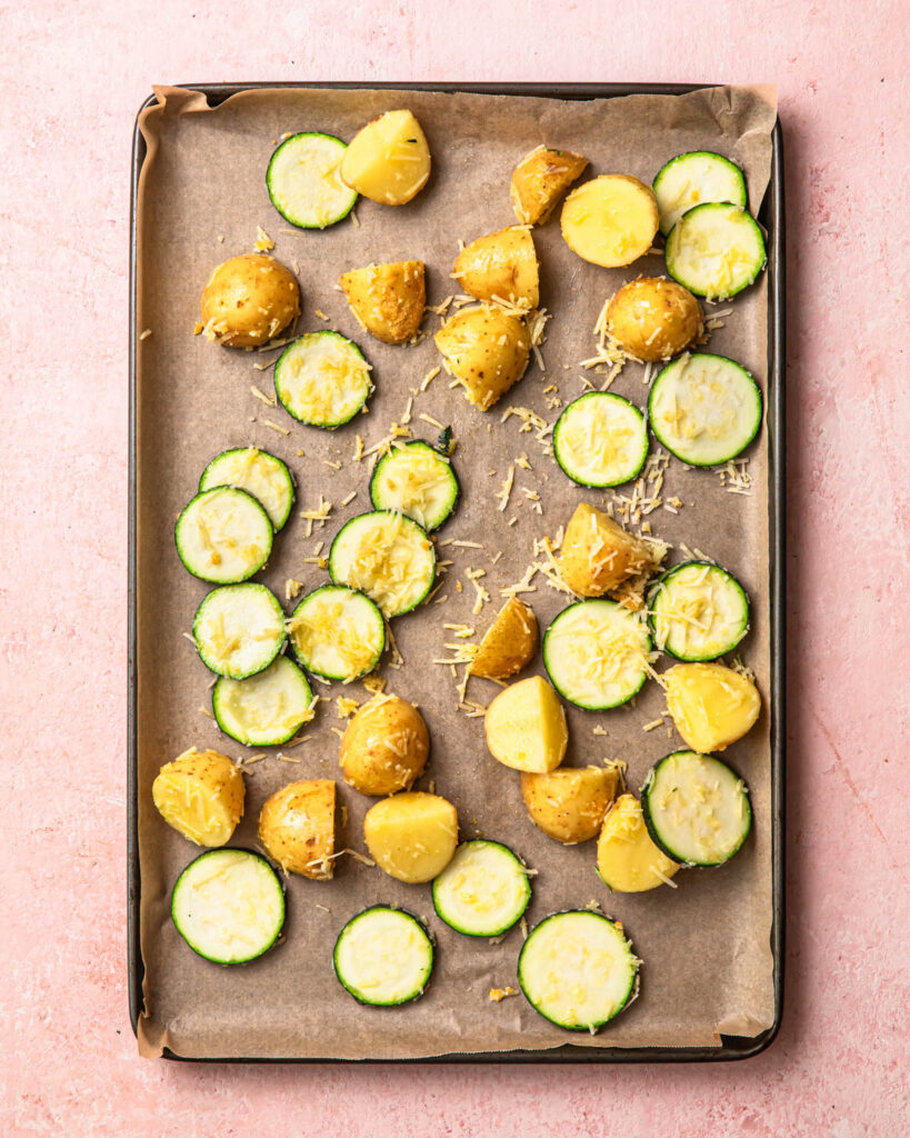 Seasoned potatoes and zucchini spread out onto a sheet pan. 
