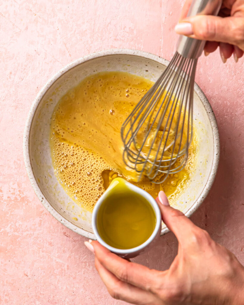Olive oil being poured into a bowl to make maple dijon dressing. 