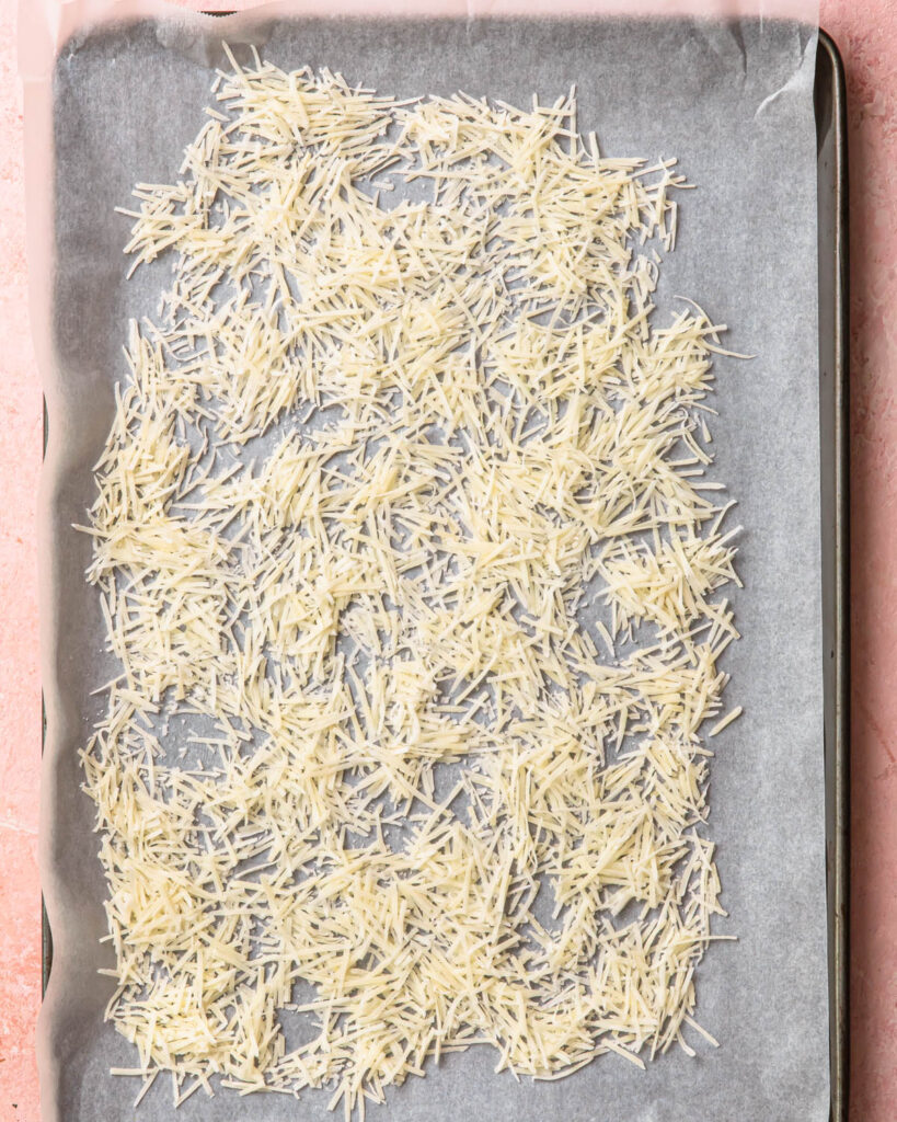 Grated parmesan cheese spread out on a large baking tray.