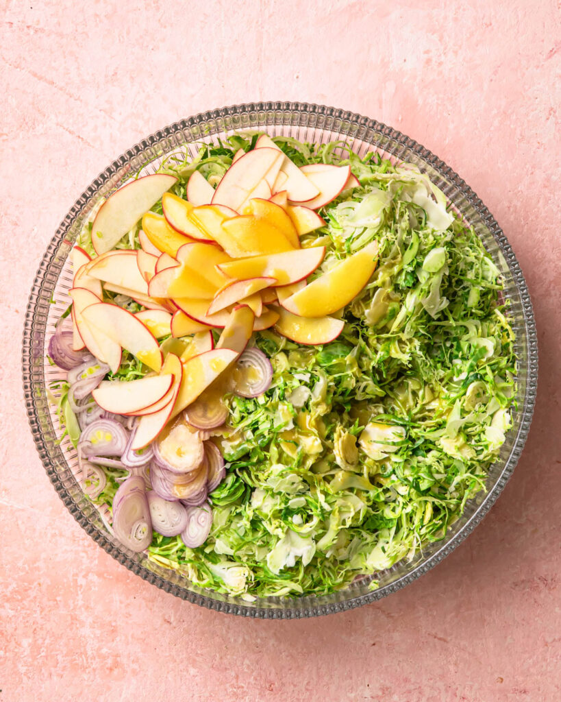 Dressing poured over ingredients for a shaved brussels sprouts salad. 