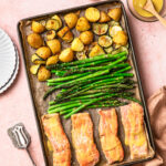 Sheet pan salmon and asparagus with parmesan potatoes sitting beside plates and sauce.