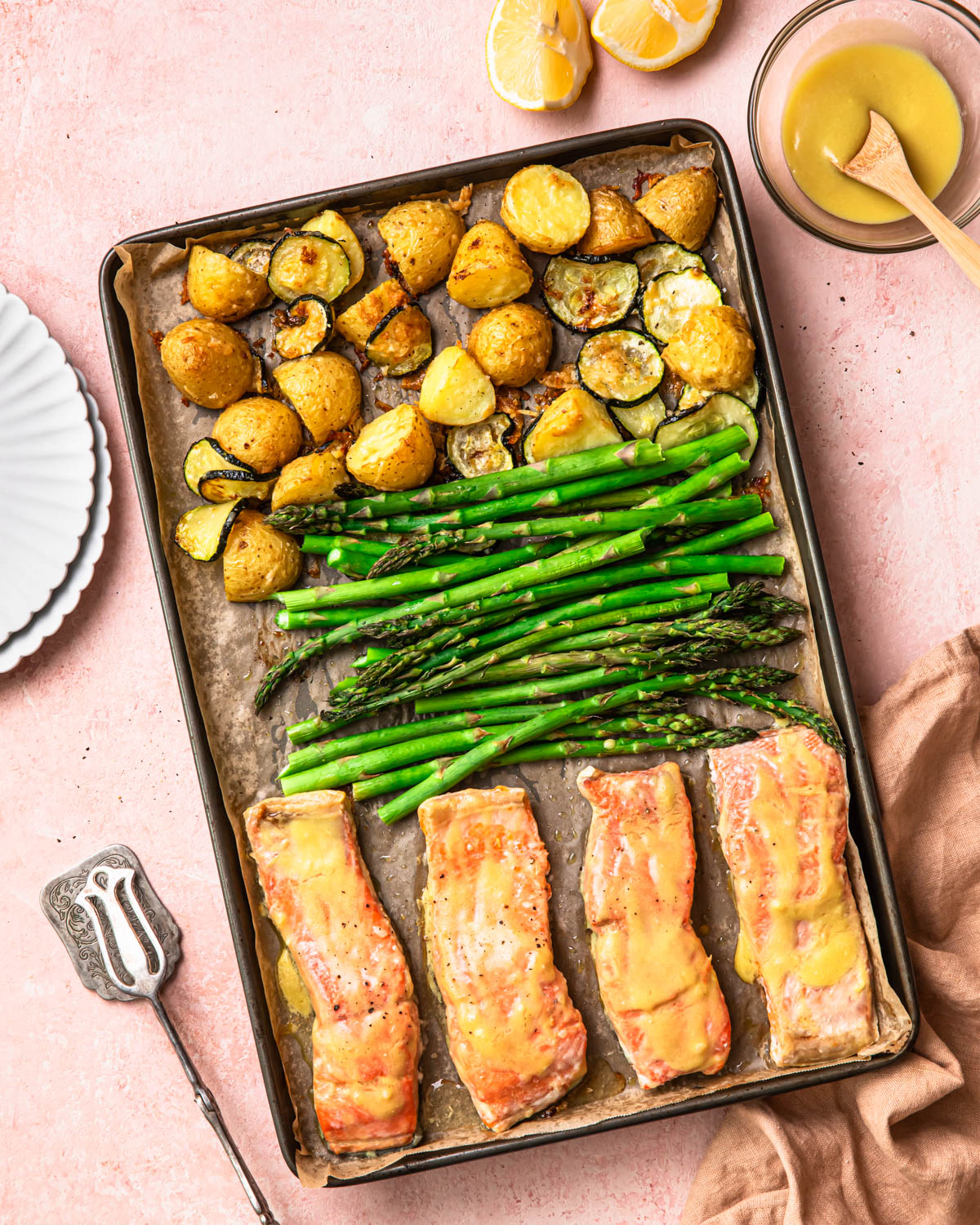 Sheet pan salmon and asparagus with parmesan potatoes sitting beside plates and sauce.
