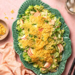 Shaved Brussels sprout salad topped with parmesan crisps on a serving platter.