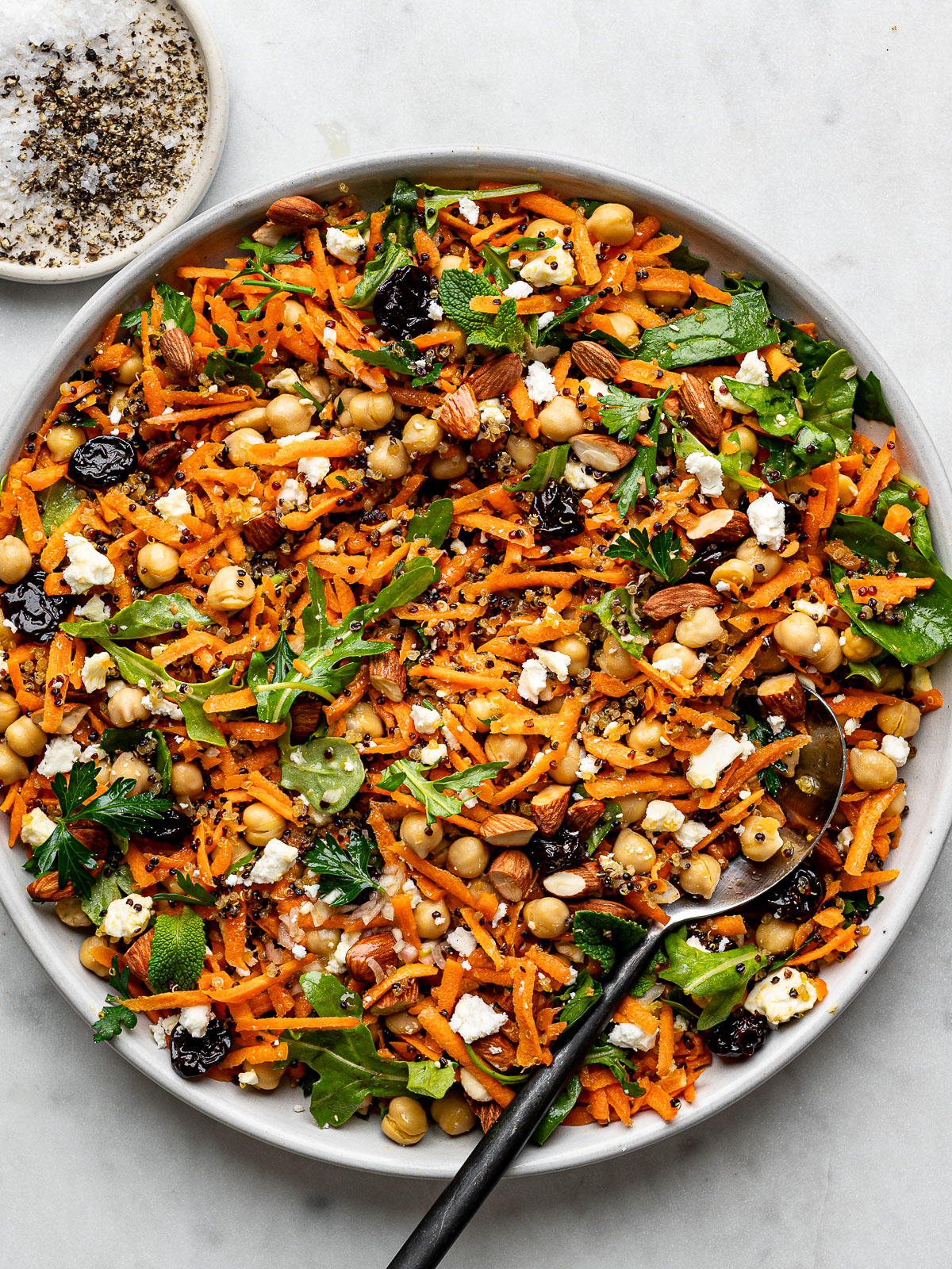 an overhead shot of carrot quinoa salad in a shallow white bowl with a tarnished silver spoon tucked in the side.