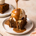 A slice of gluten free sticky date pudding topped with ice cream and warm toffee sauce being poured over the top.
