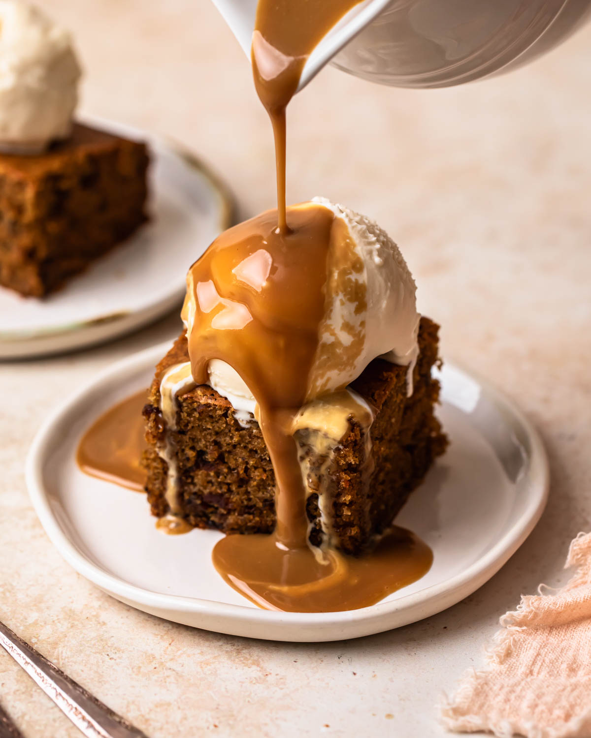 A slice of gluten free sticky date pudding topped with ice cream and warm toffee sauce being poured over the top.