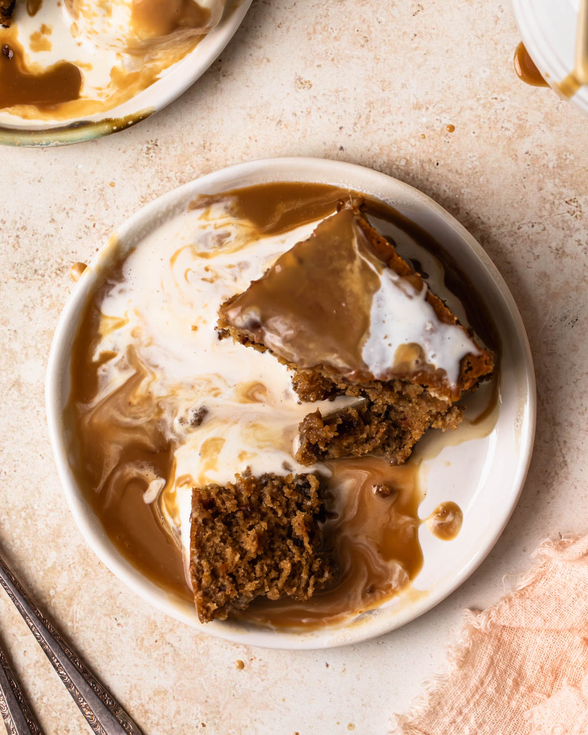 A piece of sticky date pudding broken up on a plate with melted ice cream and warm butterscotch sauce.