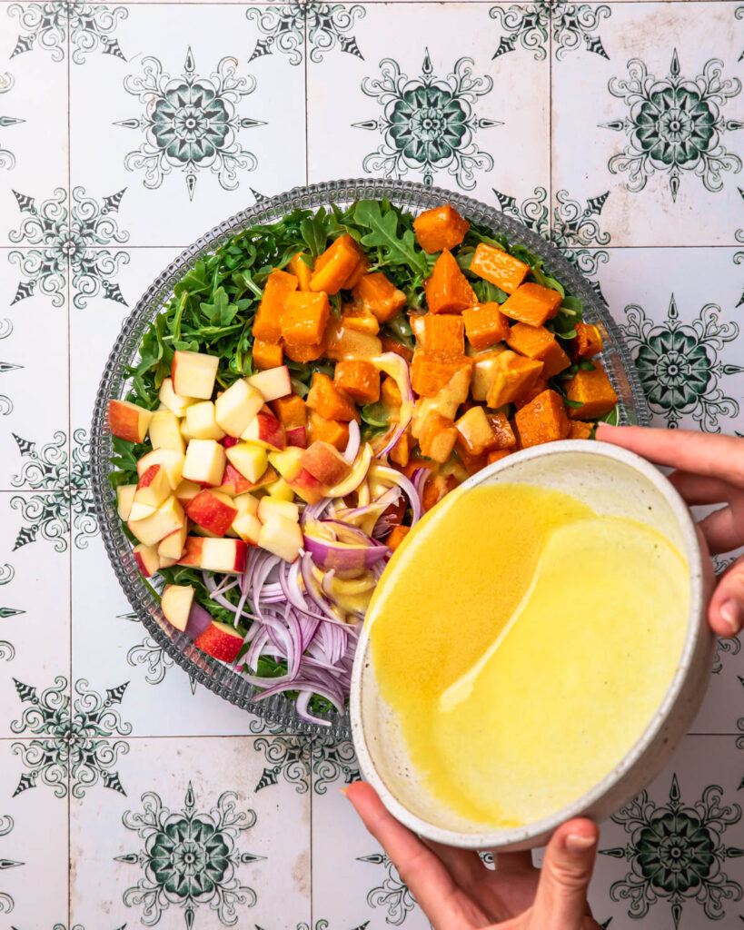 Orange dijon dressing being poured over butternut squash and feta salad.