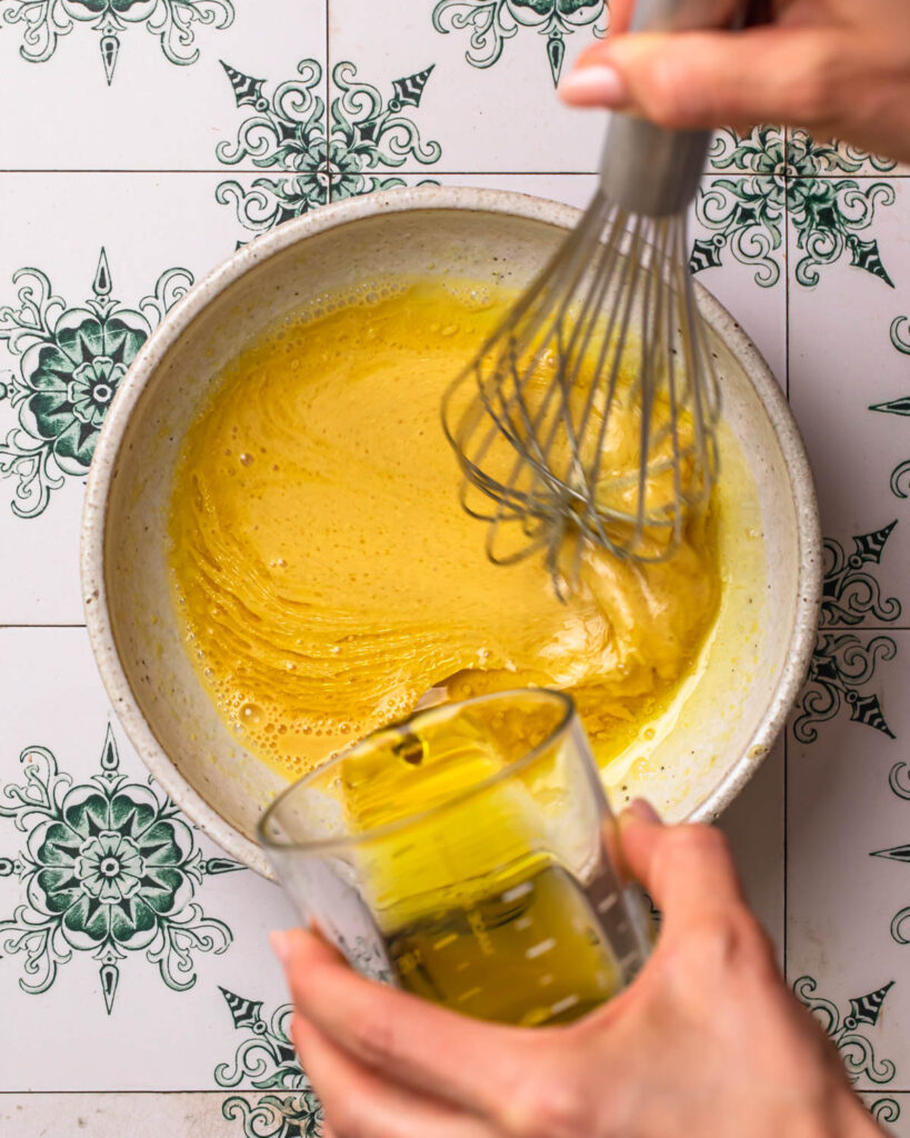 Olive oil being poured into a bowl with other ingredients to make orange dijon dressing.