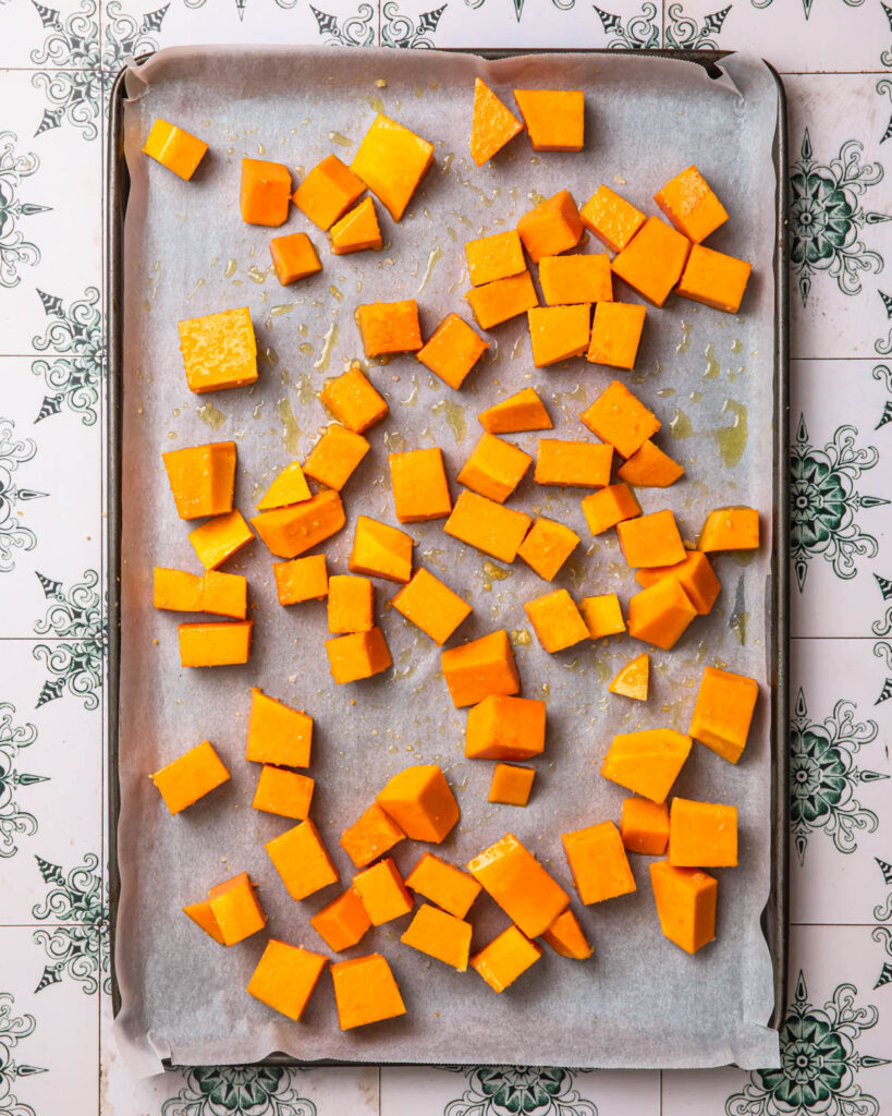 Butternut squash cubes tossed in olive oil and seasoning and spread out onto a baking sheet.