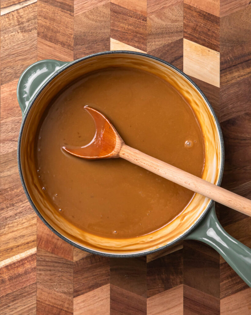 Warm butterscotch sauce in a small pan with a wooden spoon resting inside.