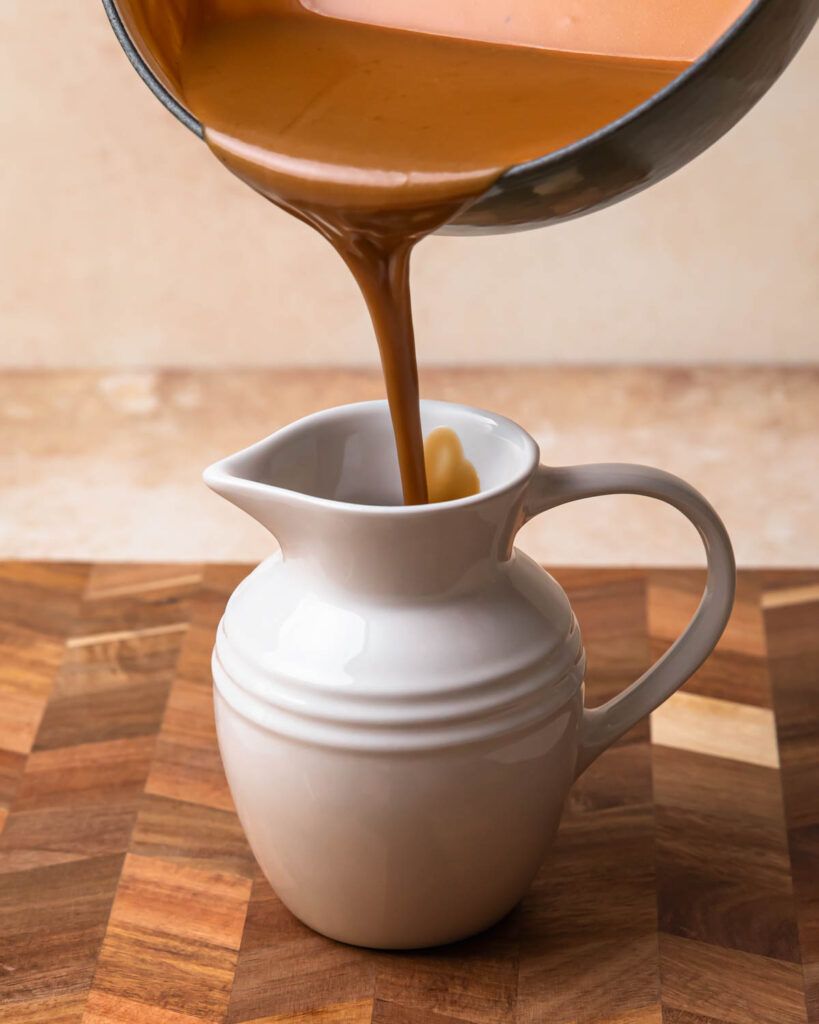 Warm butterscotch sauce being poured into a pouring jug.