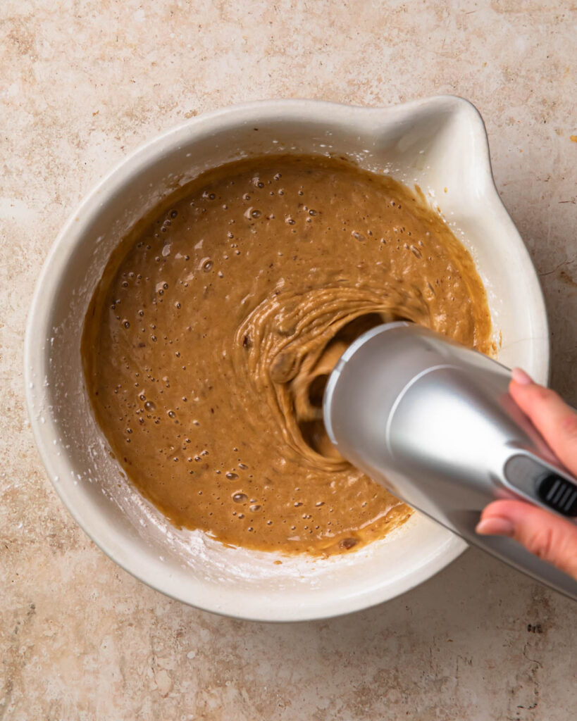 A hand holding electric beaters, mixing the sticky date pudding batter.