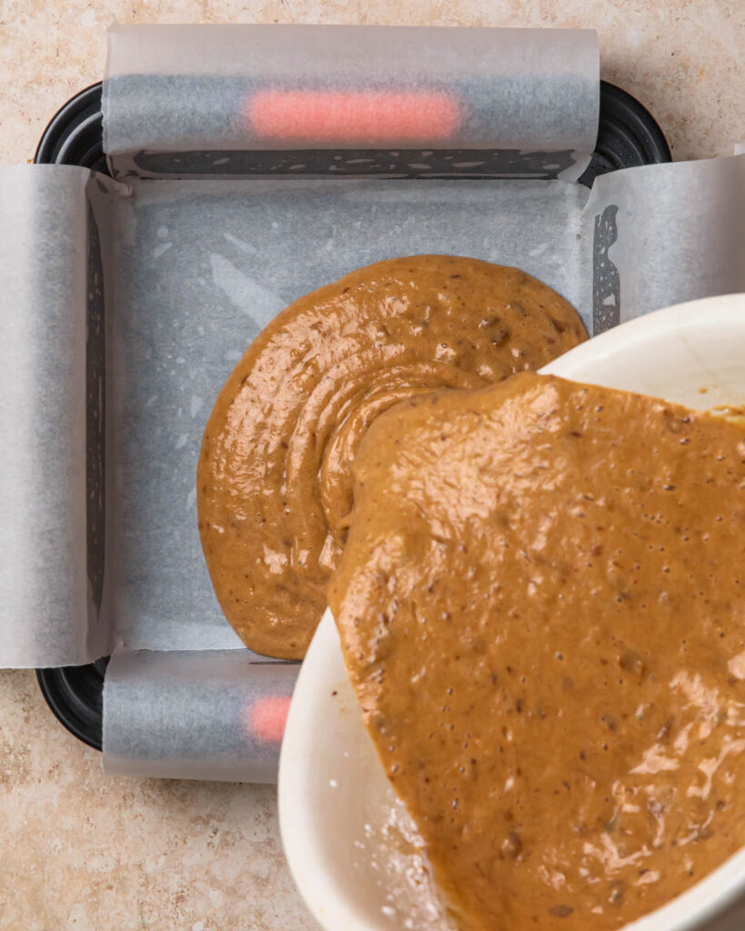 Gluten-free sticky date pudding batter being poured into a lined baking tin.