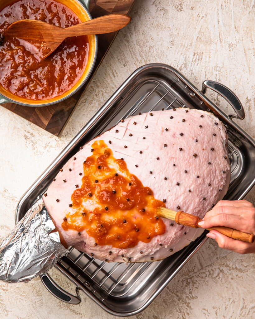 A leg ham being coated in apricot glaze. 