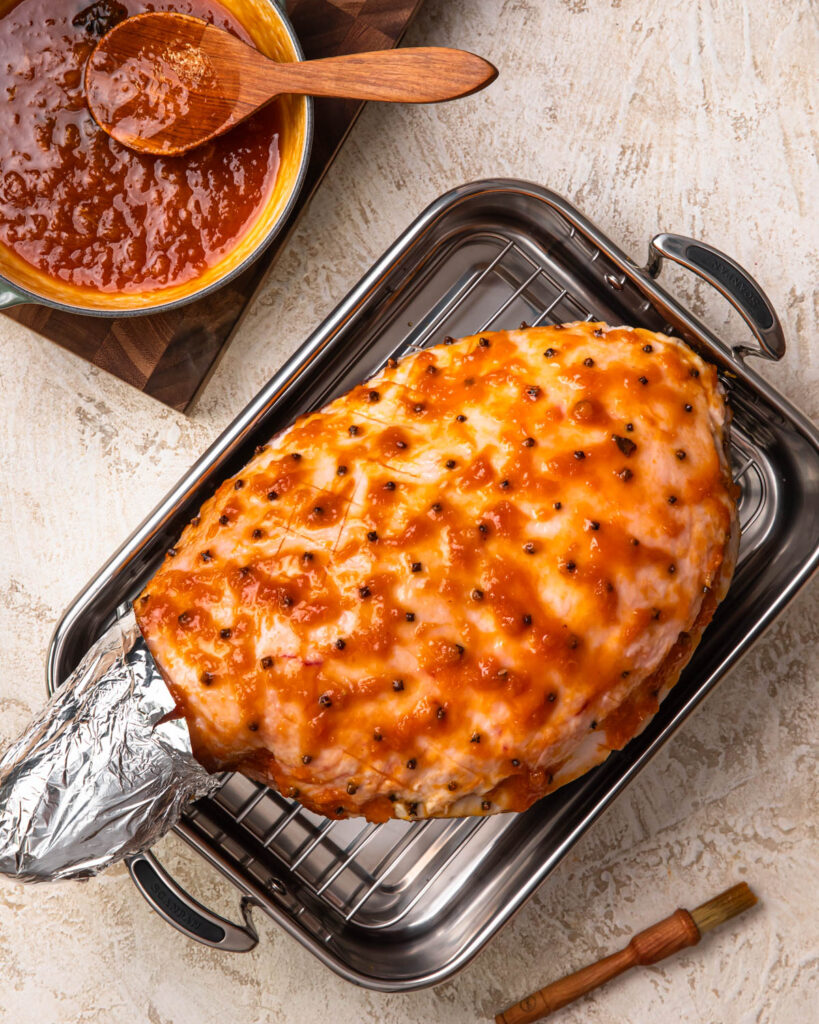 A leg ham in a roasting pan glazed with apricot glaze.