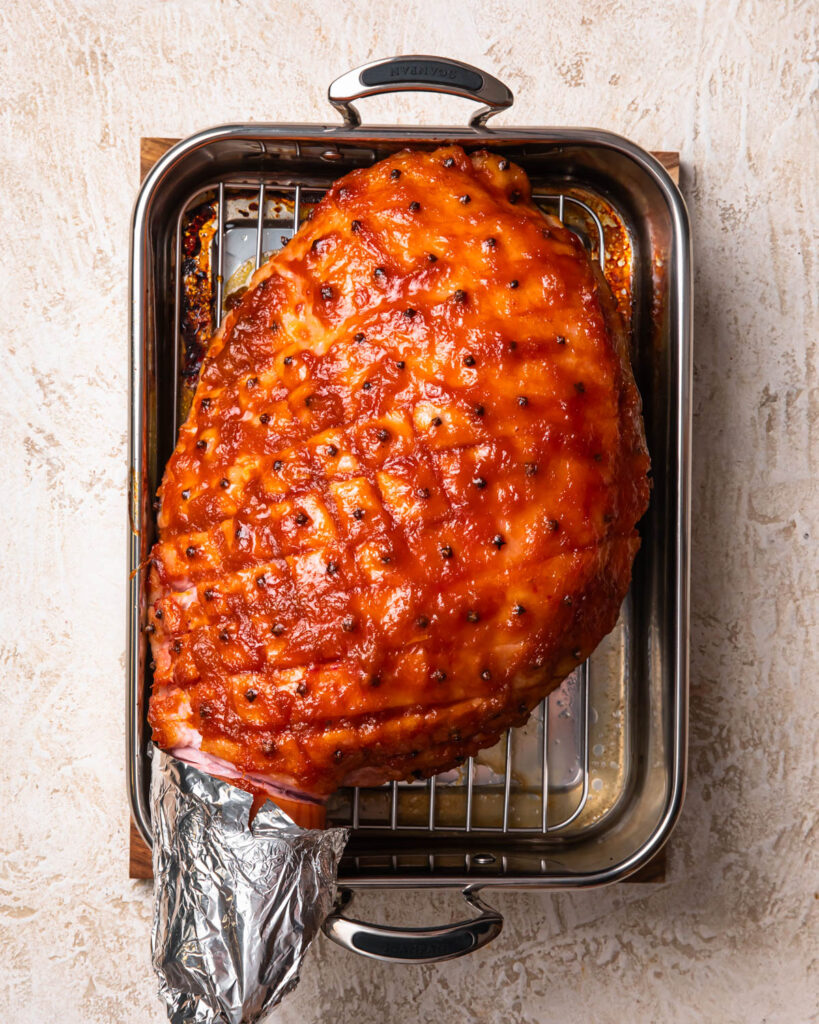 A baked apricot glazed ham in a roasting pan.
