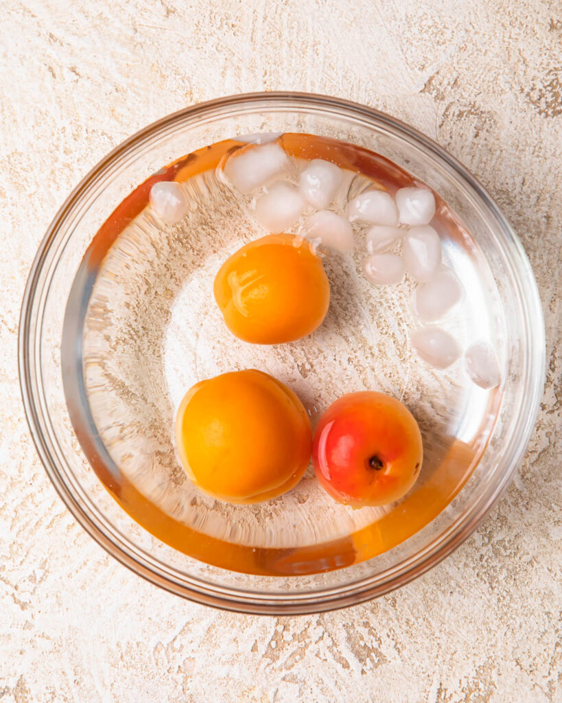 Boiled apricots in a bowl of iced water.