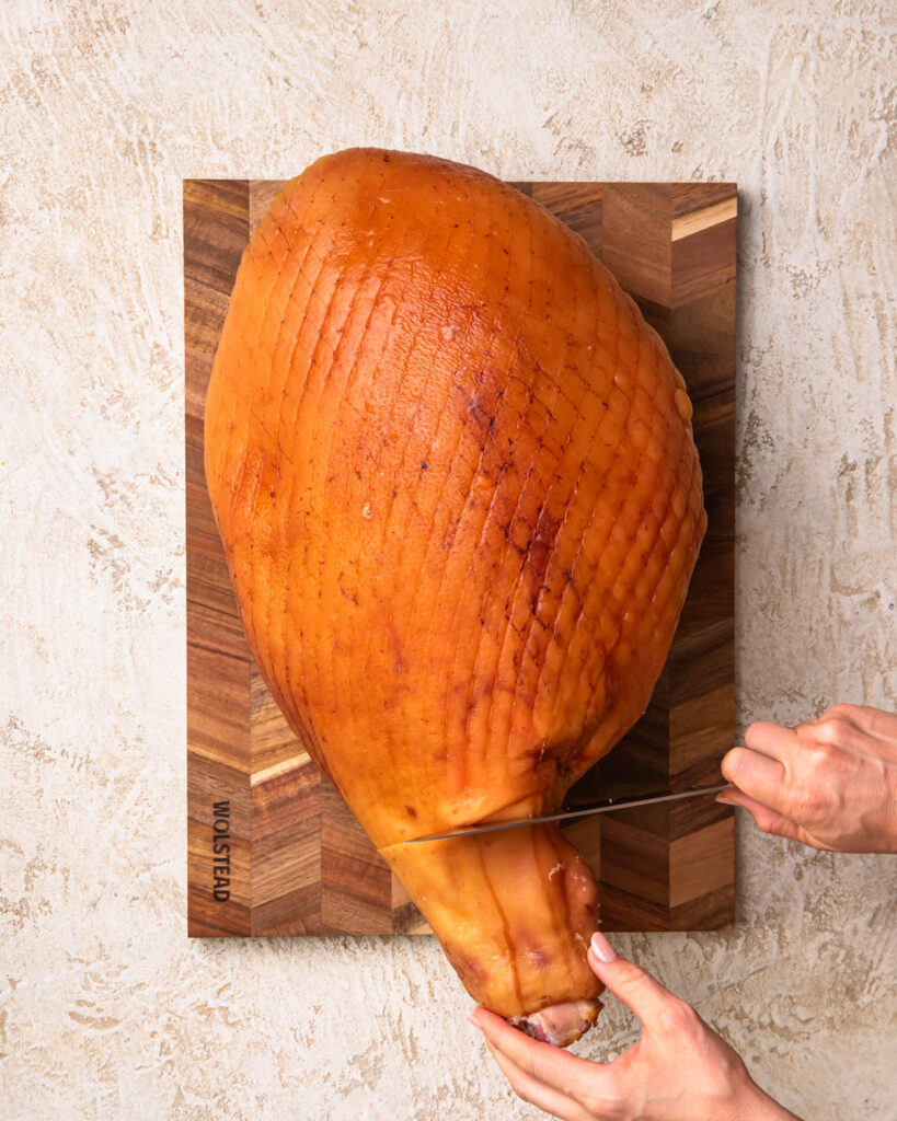 A knife slicing the skin of a leg ham near the joint. 