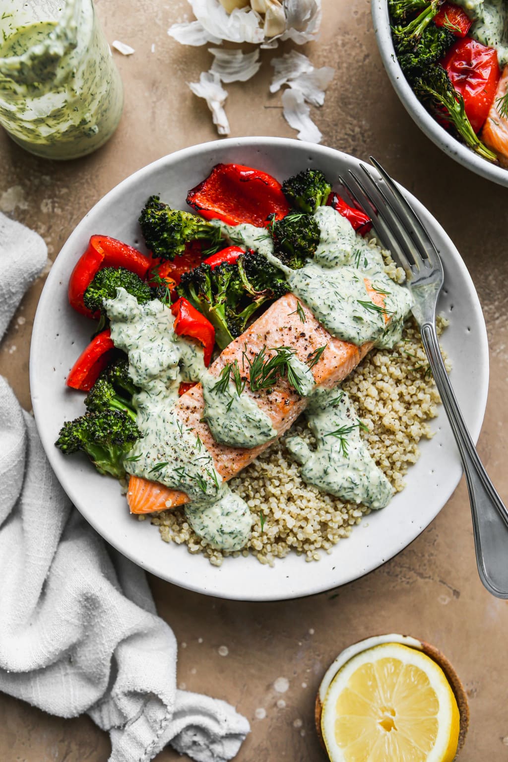an overhead shot of white bowl with roasted broccoli and red pepper and a salon filet on a bed of quinoa.