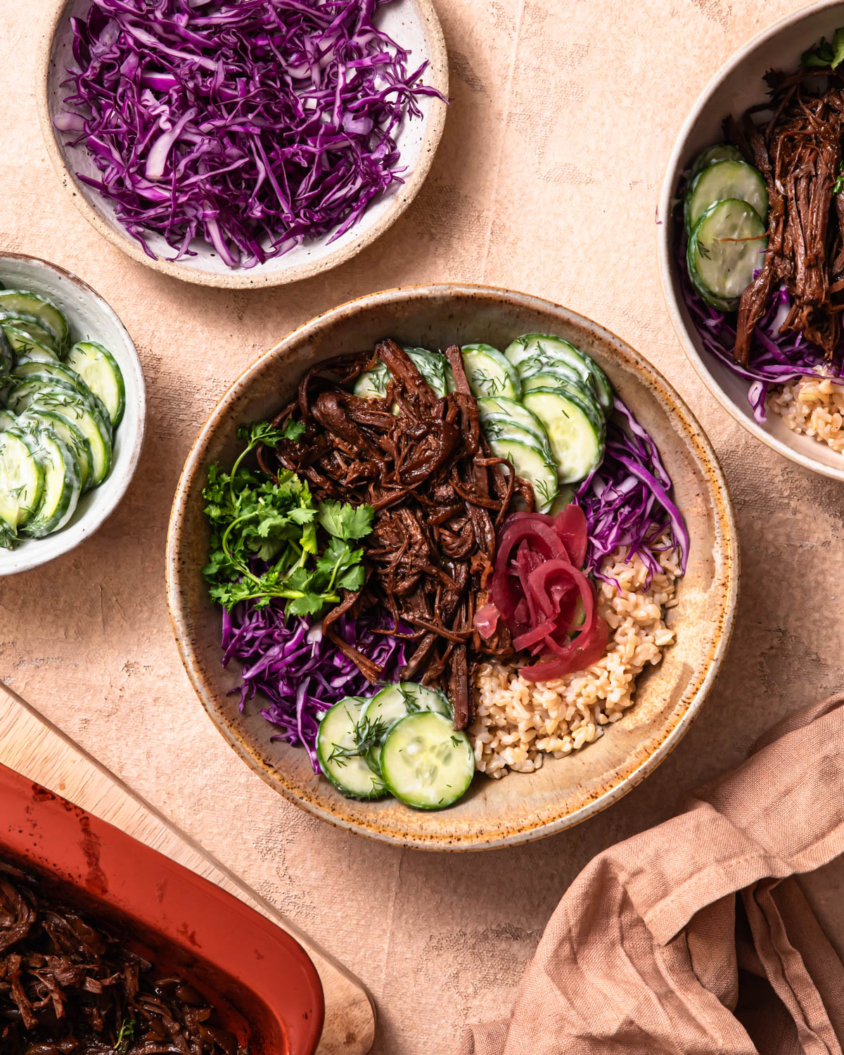 Pulled beef brisket bowls with a baking dish of pulled beef brisket in the background.