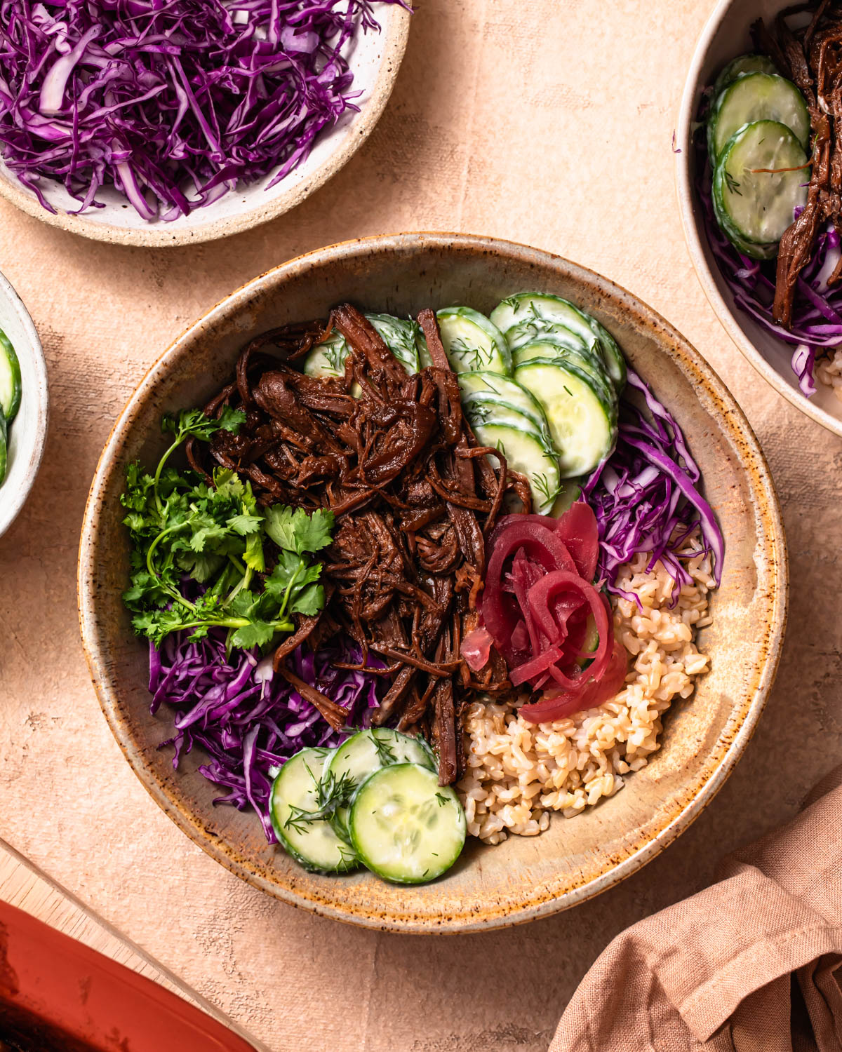 Pulled beef brisket bowls with a baking dish of pulled beef brisket in the background.