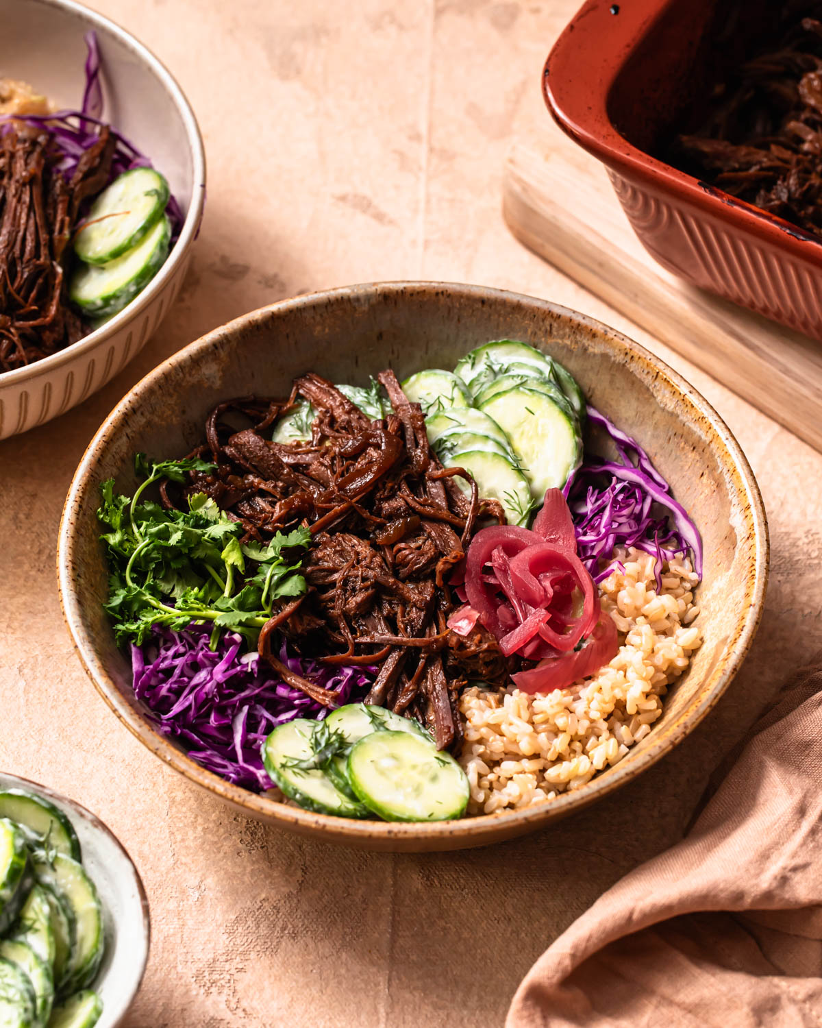 Pulled beef brisket bowls with a baking dish of pulled beef brisket in the background.