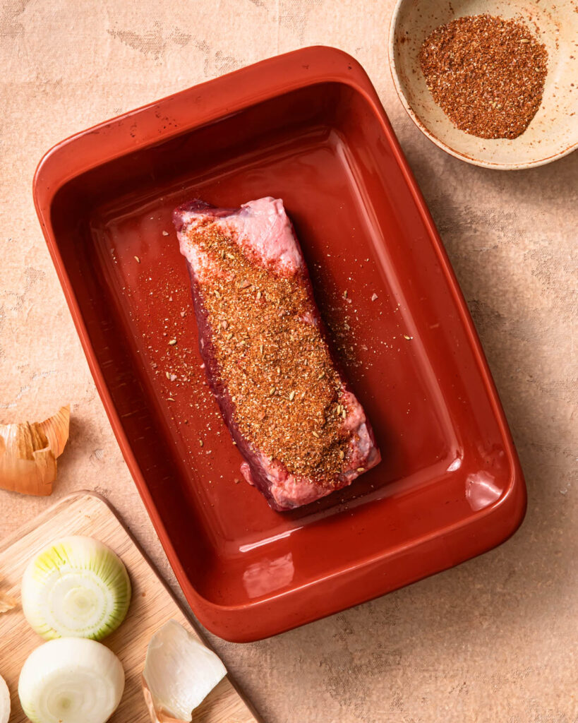 Beef brisket in a baking dish topped with spice rub.