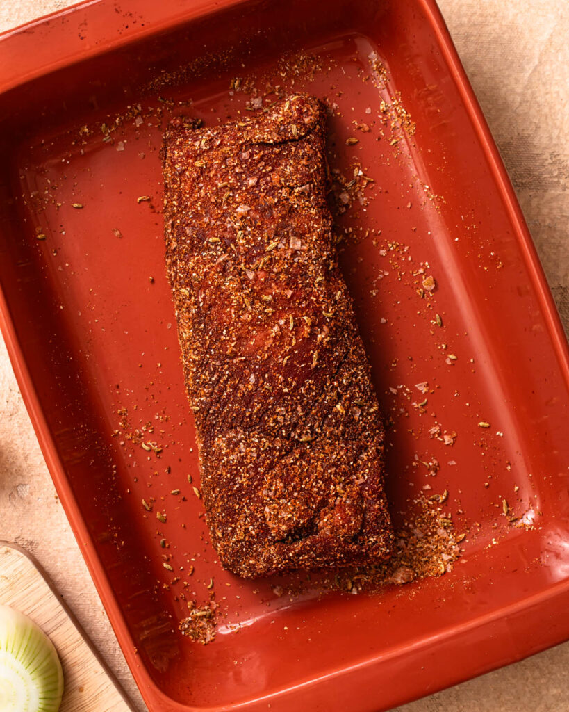 Beef brisket in a baking dish coated in a spice rub.