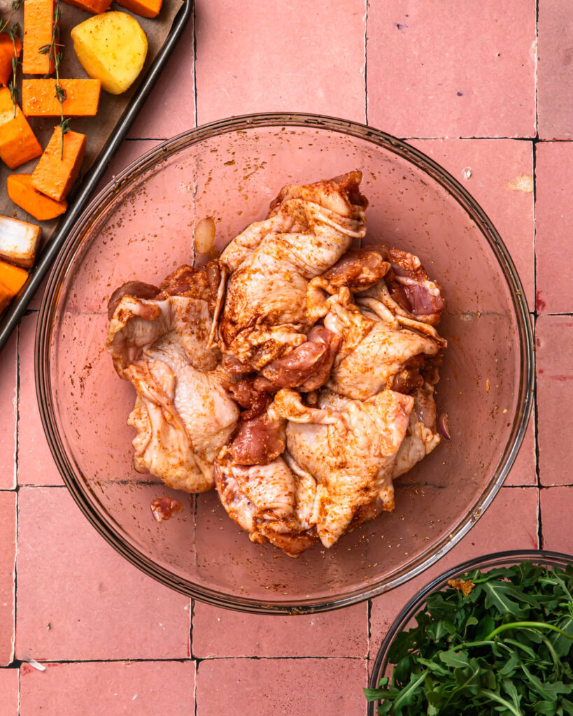 Chicken thighs in a mixing bowl, tossed in seasoning. 