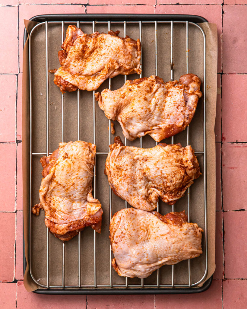 Seasoned chicken thighs on a wire rack resting on a sheet pan. 
