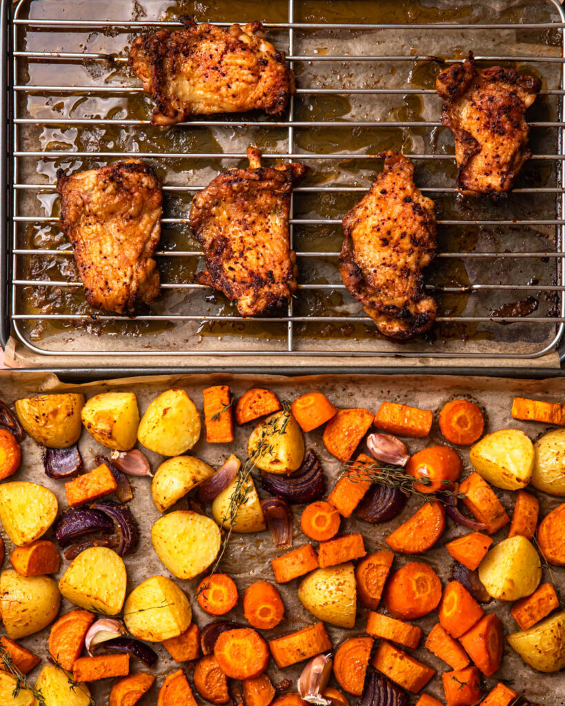 Roasted chicken thighs and vegetables on two sheet pans. 