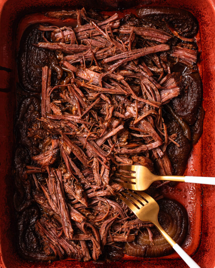Close up of pulled beef brisket in a baking dish with two forks.