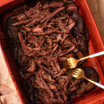 Pulled beef brisket in a baking dish with two forks.