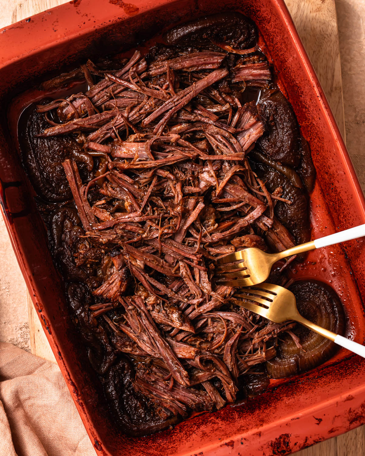 Pulled beef brisket in a baking dish with two forks.