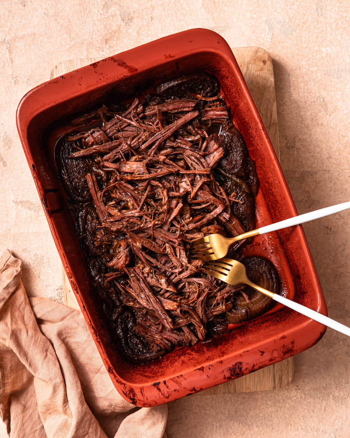 Pulled beef brisket in a baking dish with two forks.