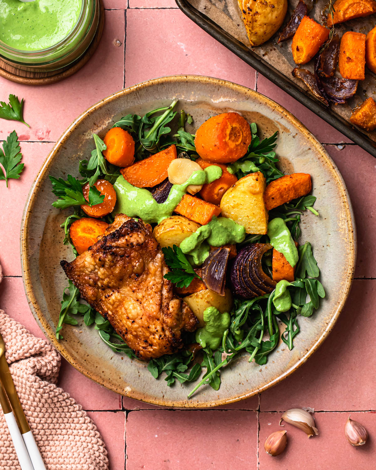 Sheet pan chicken thighs and vegetables presented on a plate over fresh greens. 
