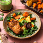 Sheet pan chicken thighs and vegetables presented on a plate over fresh greens.