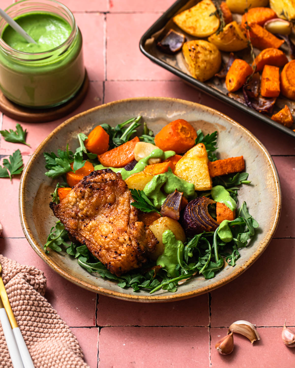 Sheet pan chicken thighs and vegetables presented on a plate over fresh greens.