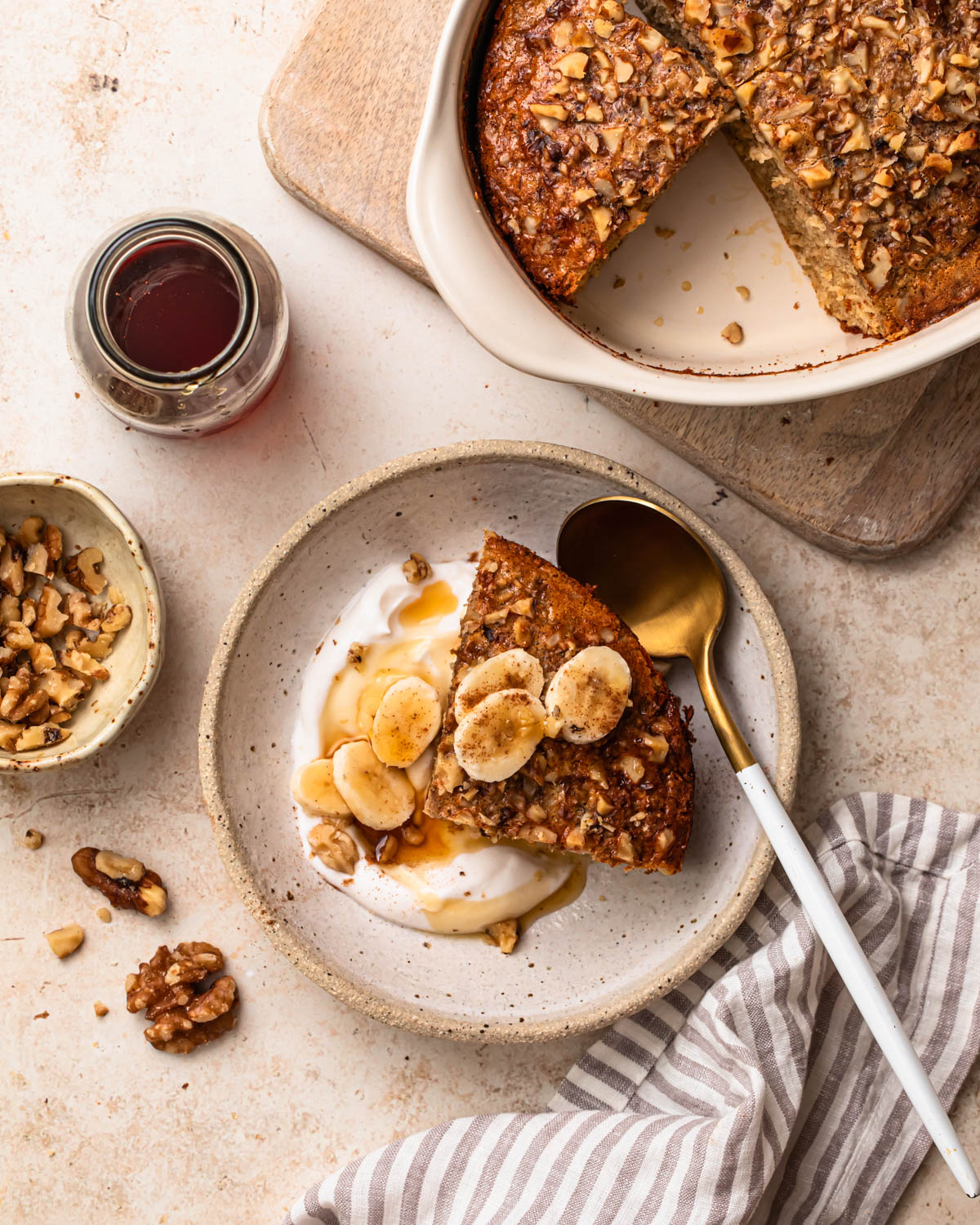 A slice of banana bread baked oats in a bowl with yoghurt, banana slices and maple syrup.