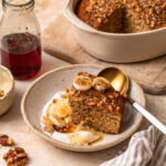 Close up photo of a slice of banana bread baked oats in a bowl with yoghurt, banana slices and maple syrup.