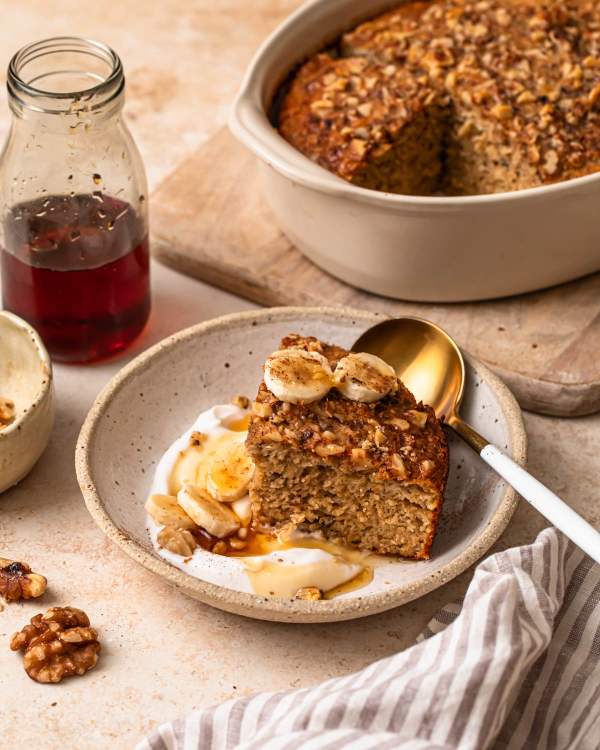 Close up photo of a slice of banana bread baked oats in a bowl with yoghurt, banana slices and maple syrup.