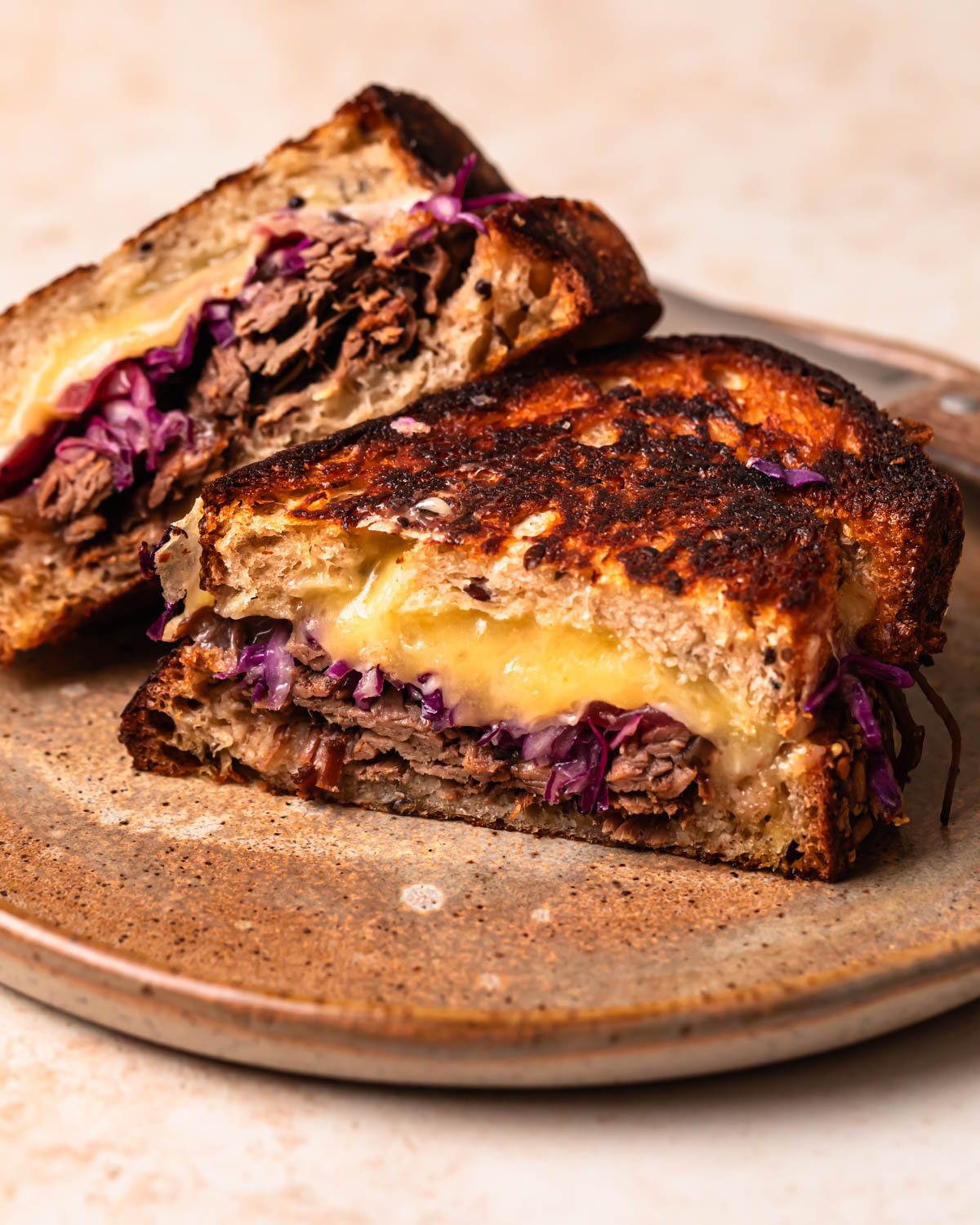A brisket grilled cheese sliced in half, with one half leaning on the other on a plate.