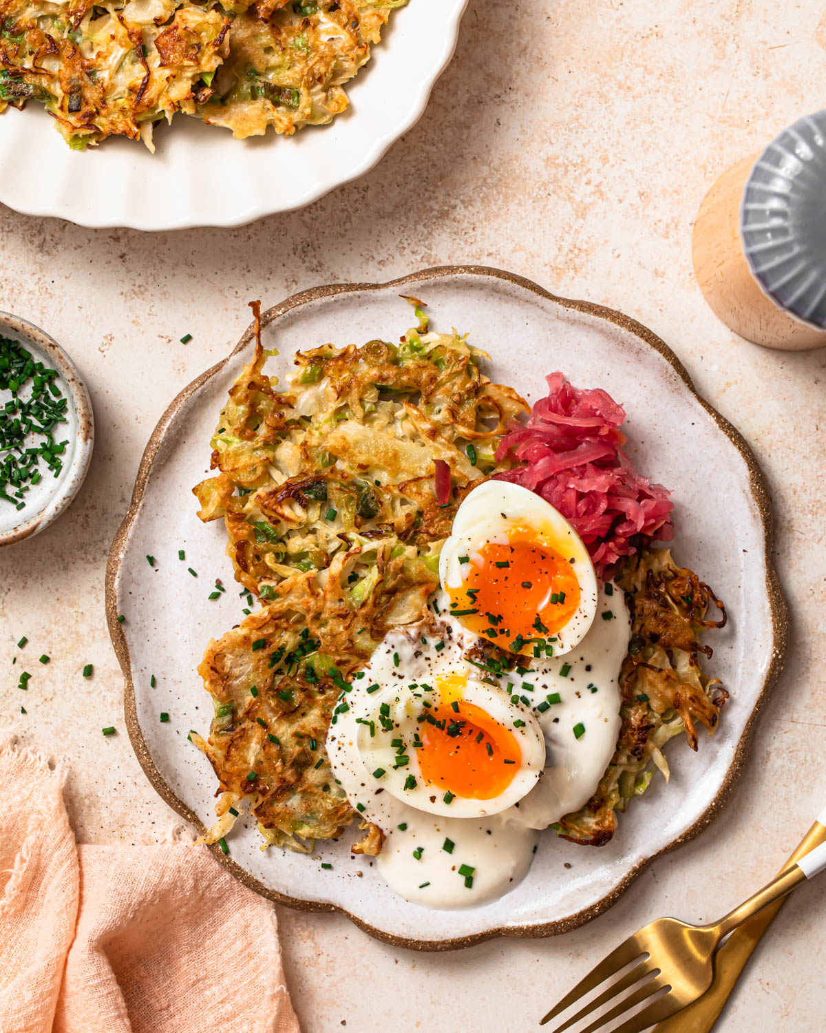 Cabbage fritters on a plate topped with garlic yoghurt, soft boiled eggs and sauerkraut.