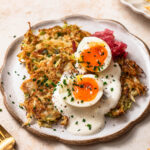 Cabbage fritters on a plate topped with garlic yoghurt, soft boiled eggs and sauerkraut.