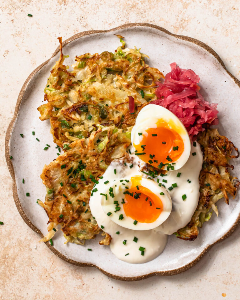 Cabbage fritters on a plate topped with garlic yoghurt, soft boiled eggs and sauerkraut.