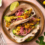 Two golden cauliflower lentil tacos resting against each other on a plate.