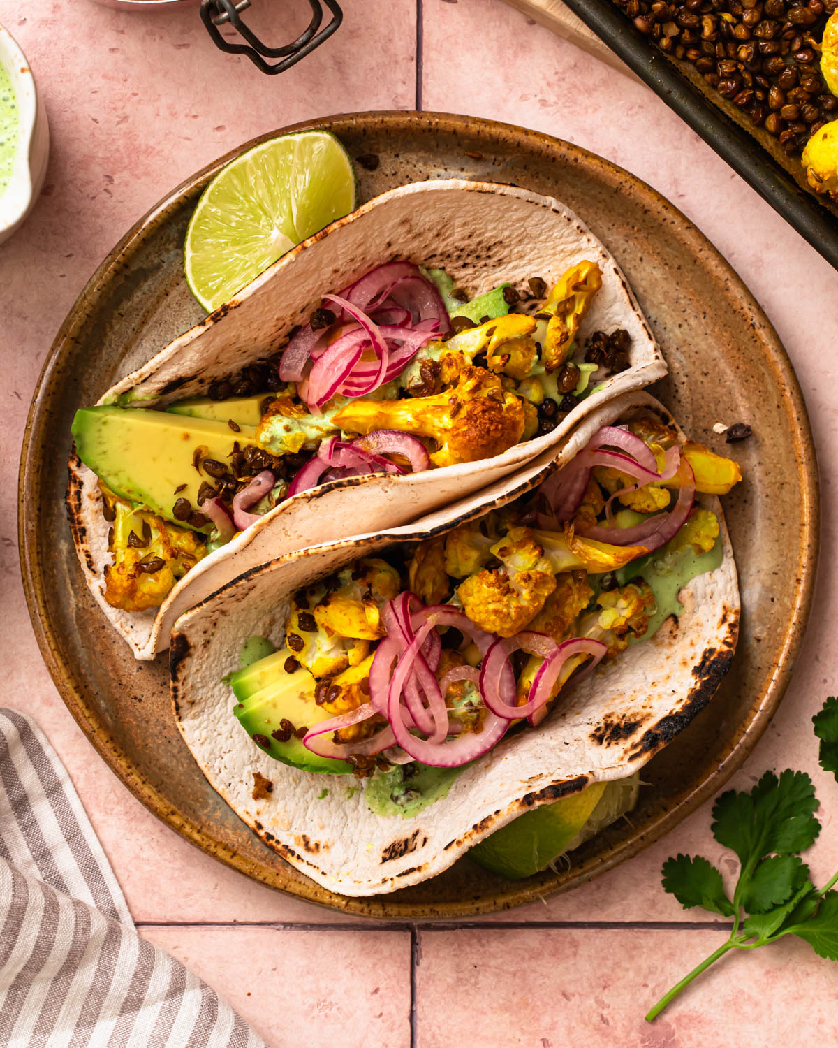 Two golden cauliflower lentil tacos resting against each other on a plate.