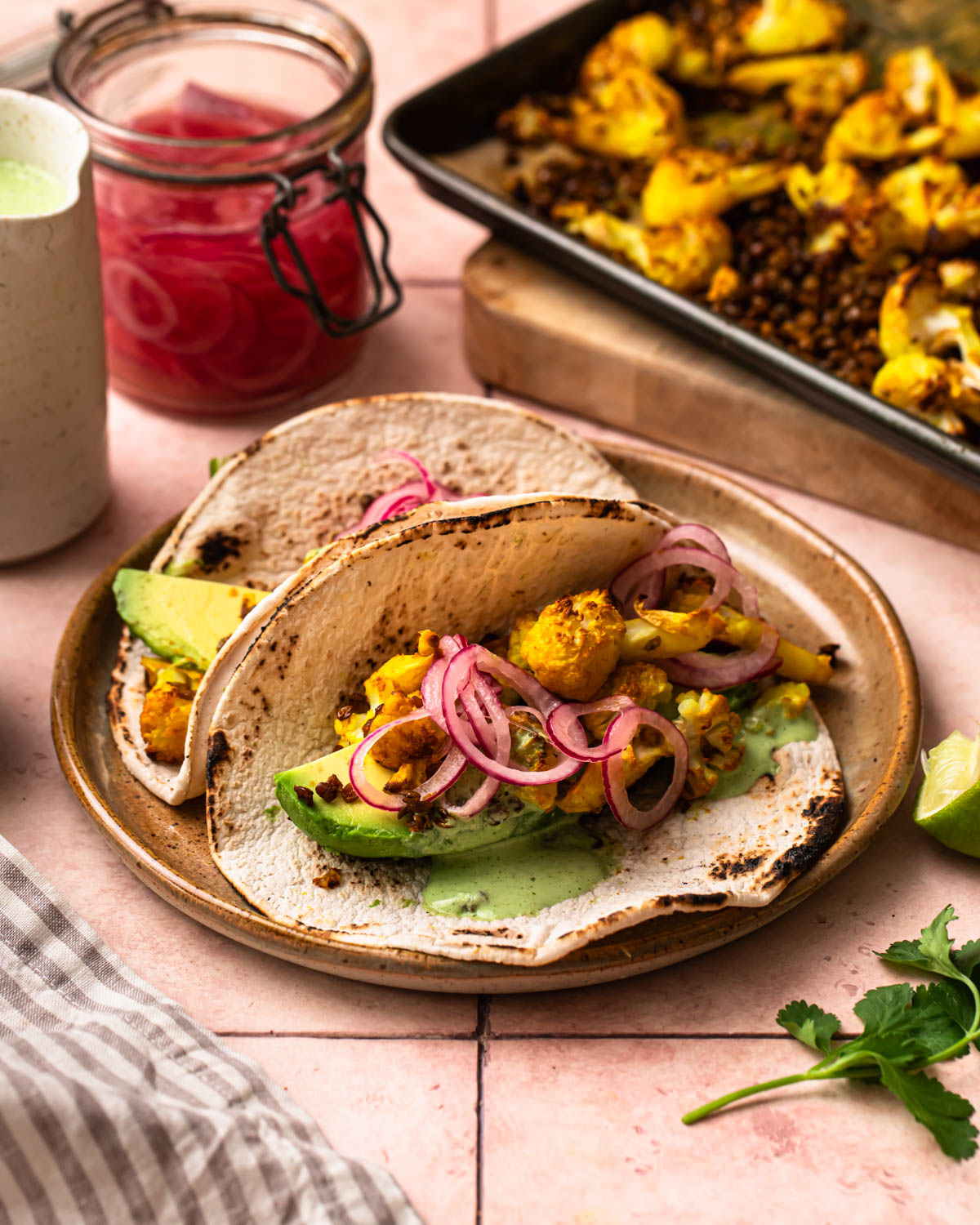Two golden cauliflower lentil tacos resting against each other on a plate.